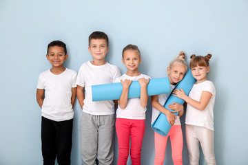 Little children with yoga mats near color wall