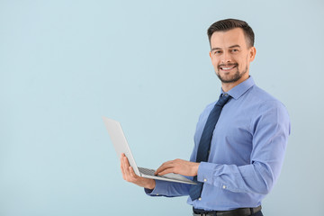 Portrait of young businessman with laptop on color background