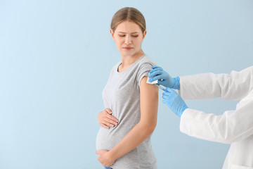 Doctor vaccinating pregnant woman on color background