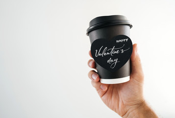 Black paper disposable cup of coffee or tea in the hand of a white man with the inscription in the heart of Happy Valentine's Day. Right hand.
