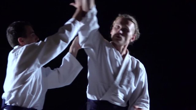 Two Masters participants of the training in special clothes of aikido hakama work out the methods of single combat on spotlights background. Slow motion. Close up.