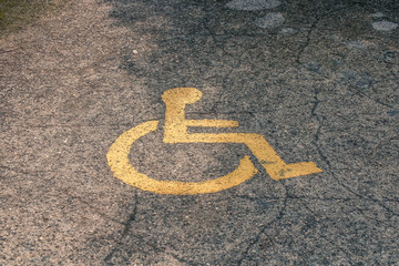 Yellow handicapped symbol of wheelchair painted on asphalt on a parking lot, sign of parking space for disabled visitors. Empty disabled parking space.