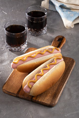 Hot dogs with mustard on a wooden board. Hot dogs served with cola on a stone table. Free space for...