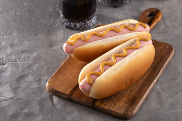 Hot dogs with mustard on a wooden board. Hot dogs served with cola on a stone table. Free space for...