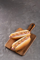 Hot dogs with mustard on a wooden board. Hot dogs served on a stone table. Free space for text