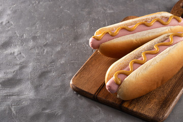Hot dogs with mustard on a wooden board. Hot dogs served on a stone table. Free space for text