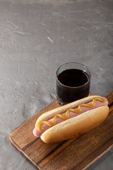 Hot dogs with mustard on a wooden board. Hot dogs served with cola on a stone table. Free space for...