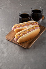 Hot dogs with mustard on a wooden board. Hot dogs served with cola on a stone table. Free space for text