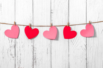 White painted wooden background with a garland of red and pink hearts. Natural rope and clothespins. Concept of recognition of love, romantic relationships, Valentine's day in grunge style. Copy space