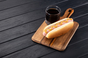 Hot dogs with mustard on a wooden board. Hot dogs served with cola on a black table. Free space for text