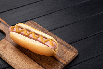 Hot dogs with mustard on a wooden board. Hot dogs served on a black table. Free space for text