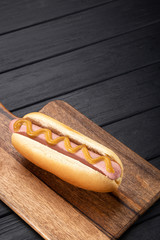 Hot dogs with mustard on a wooden board. Hot dogs served on a black table. Free space for text
