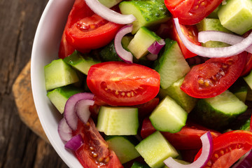 Salad of tomatoes and cucumbers in a plate on a wooden table