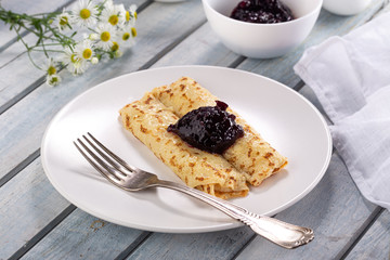 Homemade pancakes with cream cheese and berry jam on a plate, selective focus. Wooden table