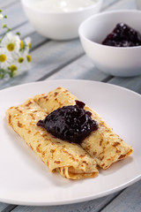 Homemade pancakes with cream cheese and berry jam on a plate, selective focus. Wooden table