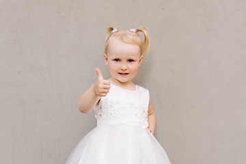 Happy baby girl in white dress on grey background