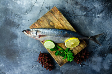 Raw mackerel on wooden cutting board  with spices, herbs and lime on black textured table.