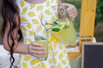 girl pours lemonade with mint from a decanter into a glass