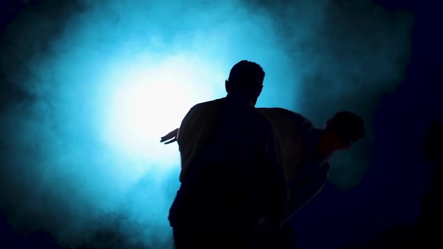 Two fighters Practicing aikido technique, silhouettes of masters in dark studio with smoke and lighting. Slow motion. Close up.