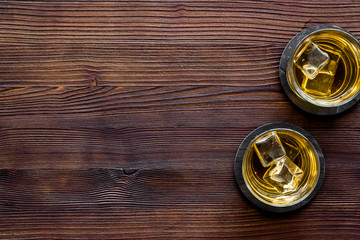 Whiskey with ice. To glasses of strong alcohol drink on dark wooden desk top-down frame copy space