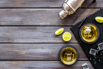 Bar background with whiskey, ice and shaker on dark wooden desk top-down frame copy space