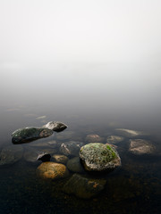 Fototapeta na wymiar Calm and minimalist landscape with beach stones and foggy horizon at autumn morning in Finland