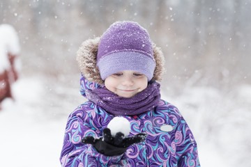 Adorable young girl having fun in beautiful winter park during snowfall. Cute child playing with a snow. Winter activities for family with kids.