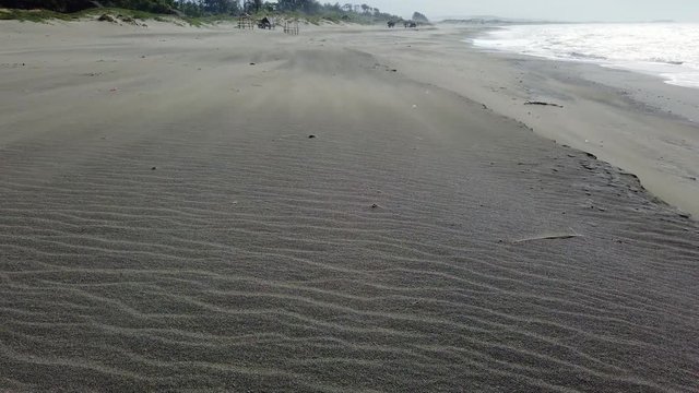 A strong wind blows on the sand on the beach. Sea surf with waves and a beautiful sandy beach. Paoay sand dune, Philippines, Luzon. Summer and travel vacation concept.
