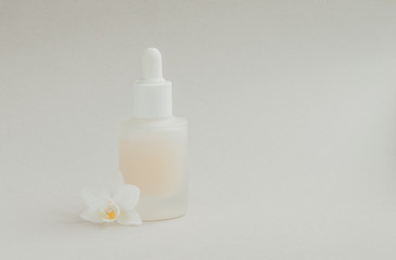 Bottle of serum for the face with a white orchid flower. Beauty product for the face on a light background.