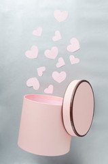 Vertical shot of opened pink box and little paper hearts on the grey surface