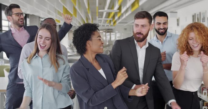 Overjoyed multiracial coworkers rejoicing corporate victory and having fun together. Cheerful young office staff dancing,smiling and moving,celebrating . Concept of people, positive emotions.