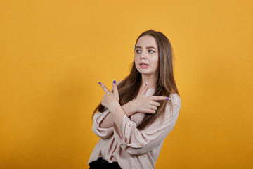 Caucasian brunette woman in fashion pastel shirt keeping hands crossed, pointing fingers aside isolated on orange background in studio. People sincere emotions, lifestyle concept.