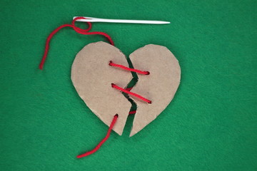 Broken cardboard heart on green felt background. Two halves of the heart sewn together in red thread. The concept of a broken heart, unrequited love. Valentine's Day stock photo with empty space