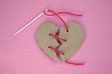 Broken cardboard heart on felt pink background. Two halves of the heart sewn together in red thread. The concept of a broken heart, unrequited love. Valentine's Day stock photo with empty space