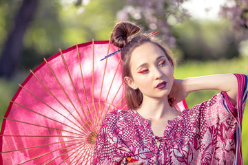 Japanese woman in kimono and with umbrella. Beauty Asian girl with a bright make-up art in green scenery park