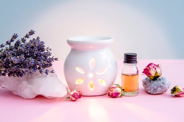 Obraz na płótnie Canvas White ceramic candle aroma oil lamp with essential oil bottle and dried flowers, crystal geodes on modern pastel pink and blue background indoors.