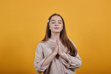 Calm caucasian brunette woman in fashion pastel shirt keeping palms together, praying isolated on orange background in studio. People sincere emotions, lifestyle concept.