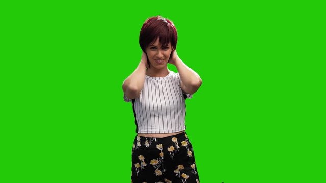 Cheerful short haired brunette female adjusting hair on green screen