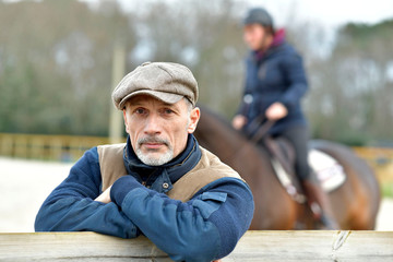 Portrait of horseman leaning on fence, horse in background
