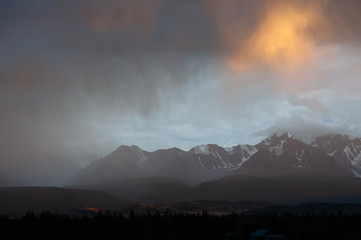 epic landscape of a giant snowy mountain range under a hurricane of rain and sun