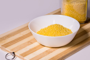 Millet groats in a white bowl on a wooden stand on a white background.