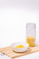 Millet groats in a white bowl on a wooden stand on a white background.