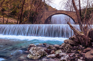 Fototapeta na wymiar The historical stone arched bridge of Palaiokarya with its two artificial waterfalls, creates a magnificent, inspiring image.