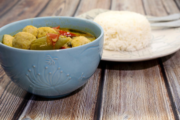 Green curry with fish balls and steamed rice on a wooden table
