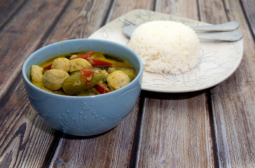 Green curry with fish balls and steamed rice on a wooden table