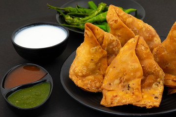 Indian Street Food Samosa or Samosas is a Crispy And Spicy Triangle Shape Snack Which Has Crisp Outer Layer of Maida & Filling of Mashed Potato, Peas And Spices. Served With Chutney, Ketchup or Curd