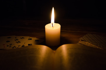 mystical atmosphere, cards, a book, a lighted candle in the dark on a wooden table. Esoteric...