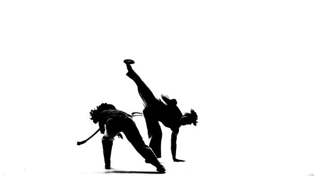 Silhouettes of Woman and man are practicing capoeira in white background of studio. Afro-Brazilian martial art that combine elements of dance.