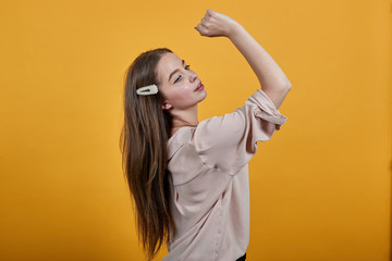 Cheerful caucasian brunette woman in fashion pastel shirt keeping fist above head, staying sideways isolated on orange background in studio. People sincere emotions, lifestyle concept.