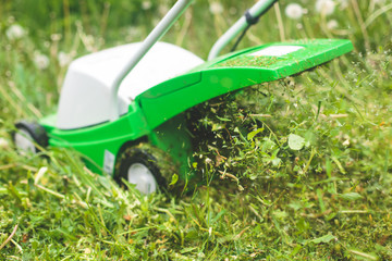 A process of lawn mowing, concept of mowing the lawn, lawnmower cutting grass with gardening tools and green grass around